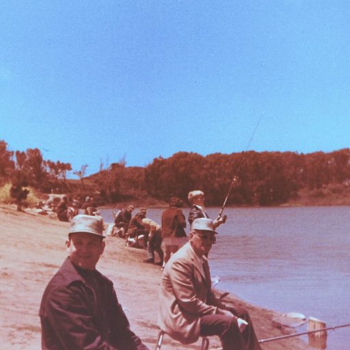 Fishing Lake Merced north shore in the early 1970s, several people are sitting on folding chairs with their fishing rods in front of them.